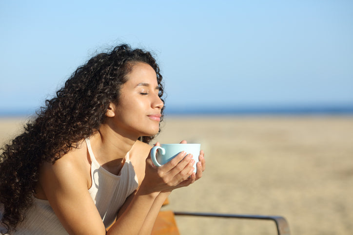 girl sitting on beach with cup being mindful